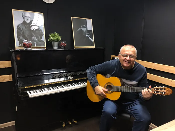 Мужчина играет на классической гитаре, рядом пианино