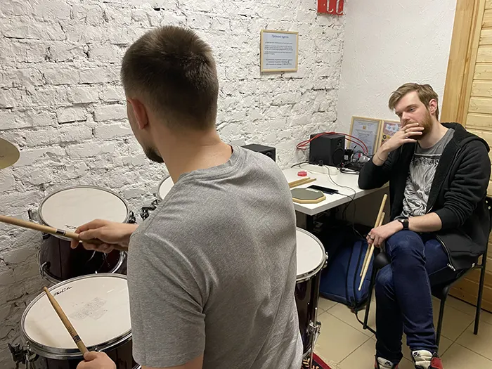 Ученик за барабанной установкой, преподаватель слушает рядом